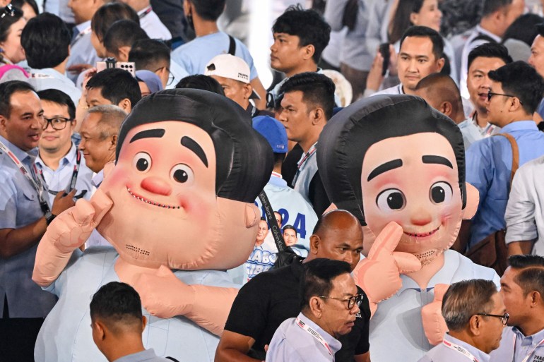 People walk past mascots depicting presidential candidate and Indonesia’s Defence Minister Prabowo Subianto (L) and vice presidential candidate Gibran Rakabuming Raka during their election campaign event at the Indonesia Arena in Jakarta on February 5, 2024. (Photo by Adek BERRY / AFP)