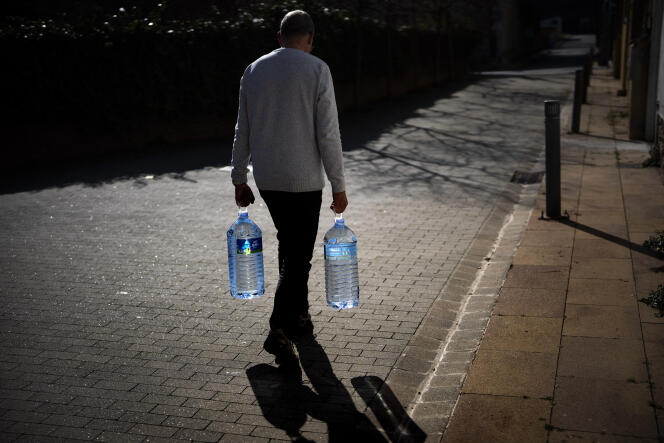 رجل يحمل عبوتين مملوءتين بالمياه إلى نبع طبيعي في جوالبا بمنطقة برشلونة (إسبانيا)، 31 يناير 2024. 